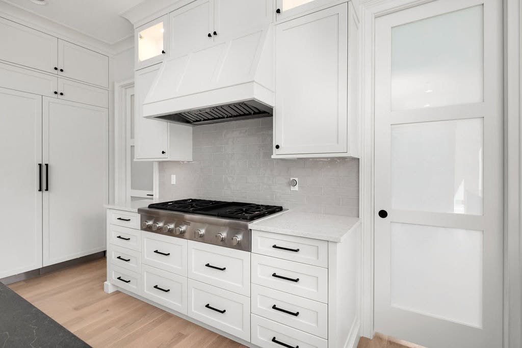 Modern white kitchen with black hardware, stainless steel gas stove, white cabinets, and light wood flooring.