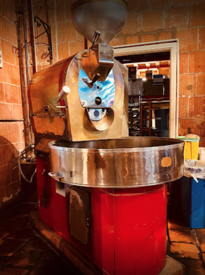 Vintage coffee roasting machine with a large metal cooling tray in a brick-walled workshop