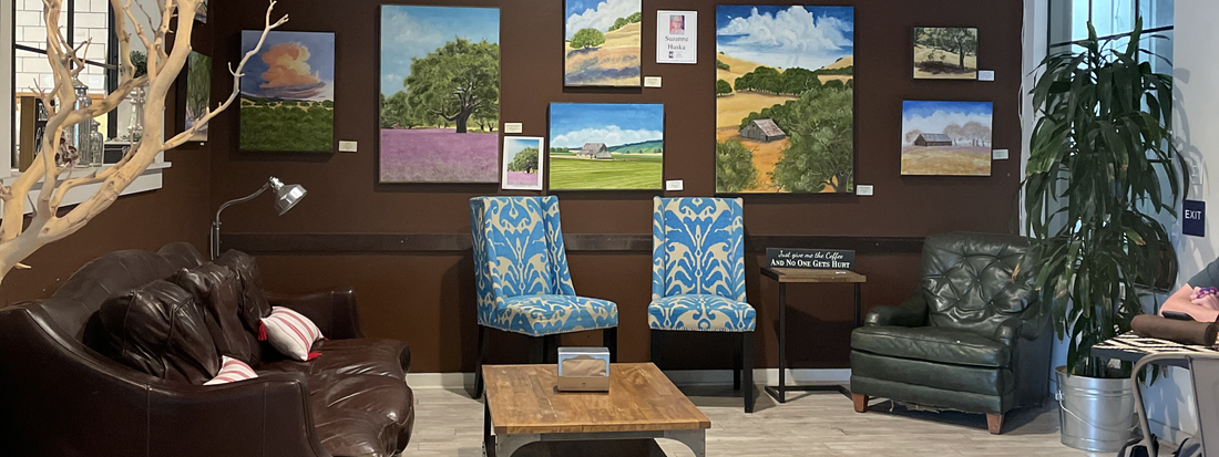Hotel lounge with leather sofas, patterned armchairs, coffee table, potted plant, and colorful landscape paintings on a dark wall
