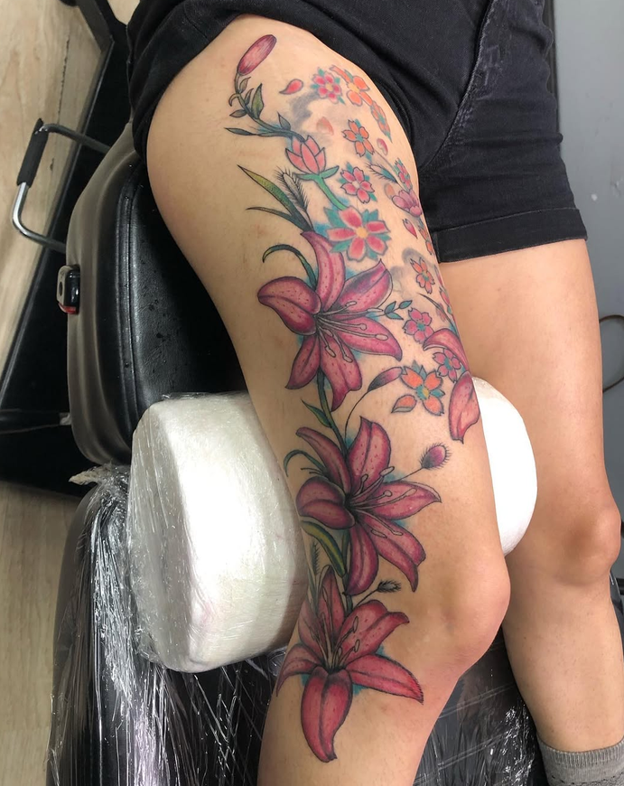 Tattoo of pink lilies and small colorful flowers on a person's thigh