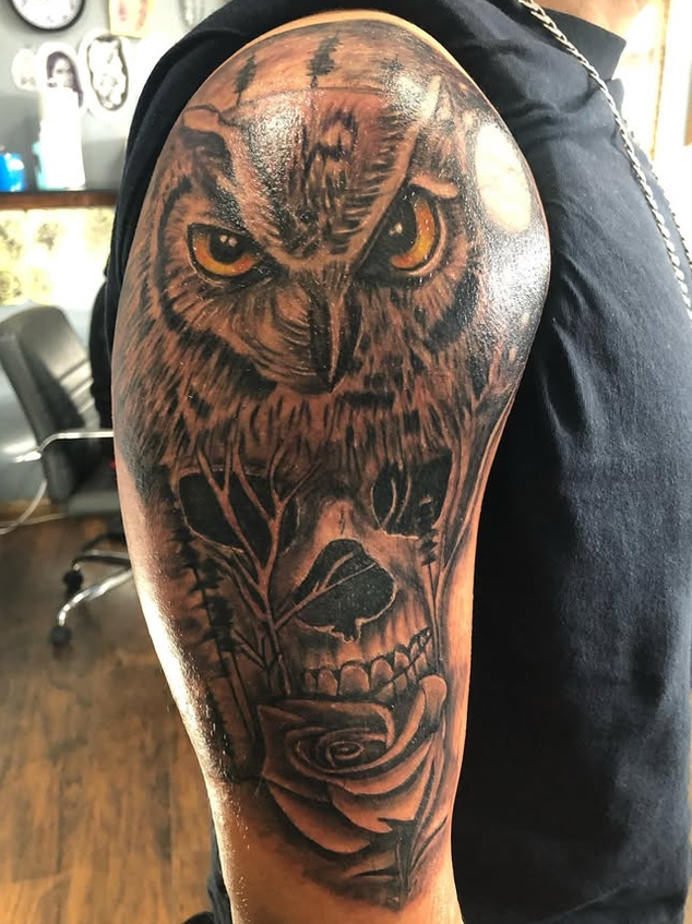 Tattoo of an owl, a skull with a rose in its mouth, and additional floral elements on a person's upper arm.