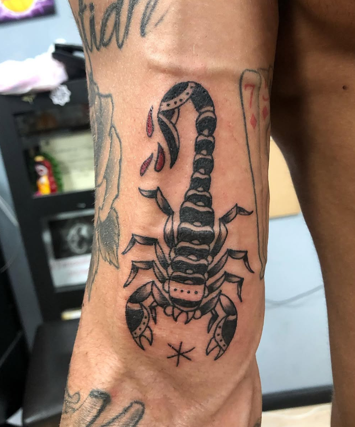 Tattoo of a black and grey scorpion on a person's arm with some red ink accents.