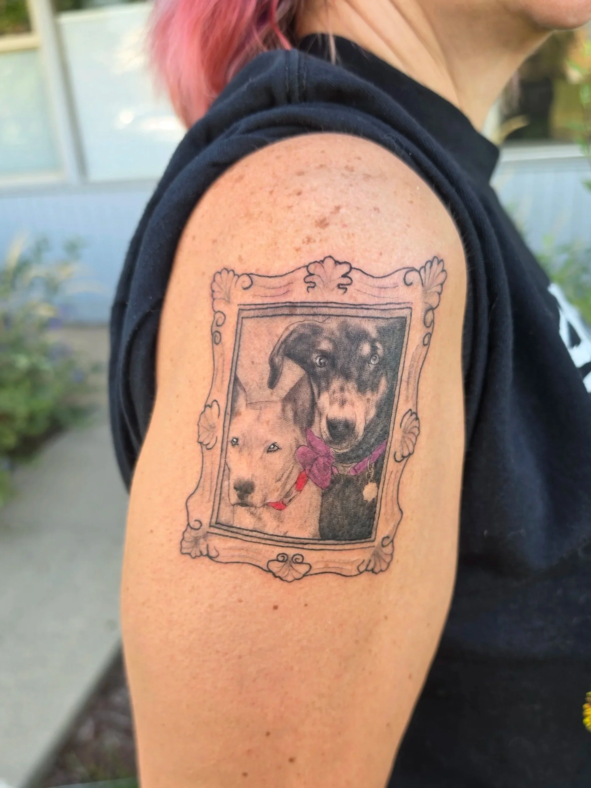Tattoo of a dog and a pig inside an ornate frame on an upper arm.