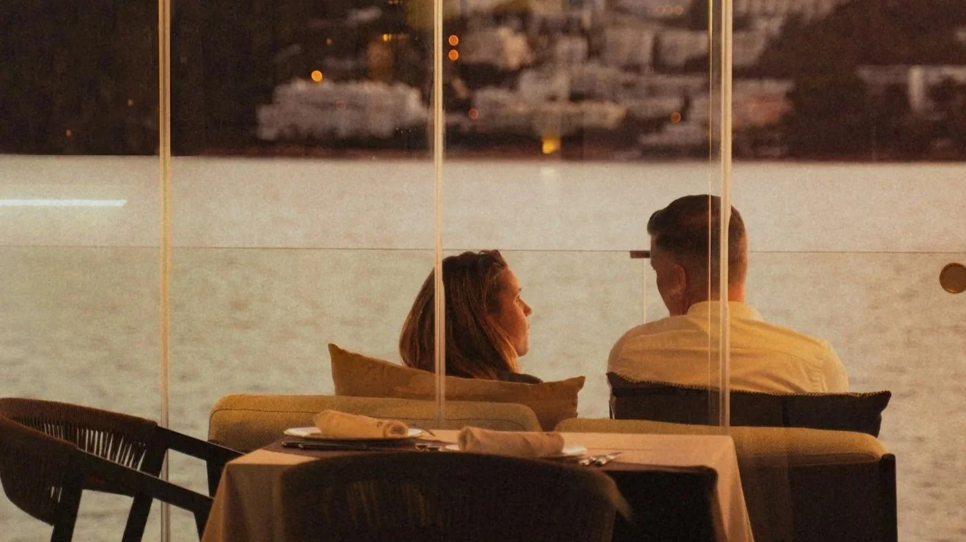 Couple seated at a waterfront restaurant table at sunset
