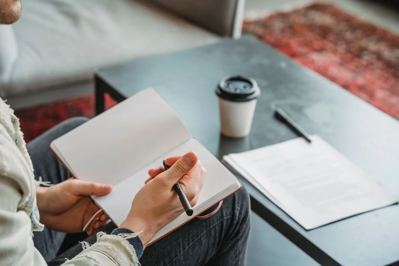 Person writing in an open notebook beside a coffee cup and papers on a table