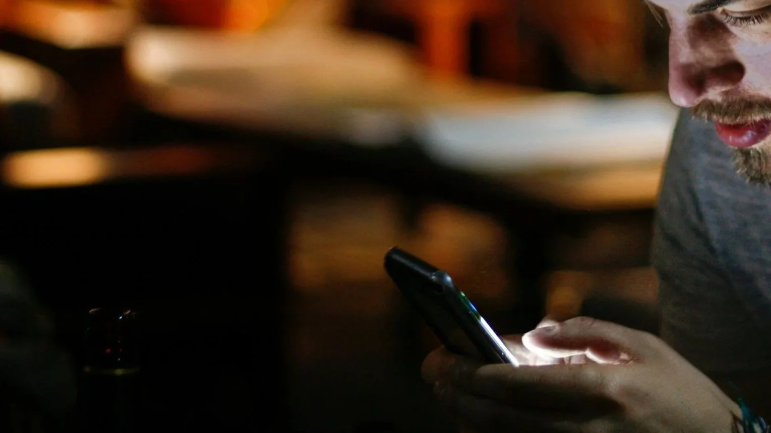 Man using a smartphone in a dimly lit bar