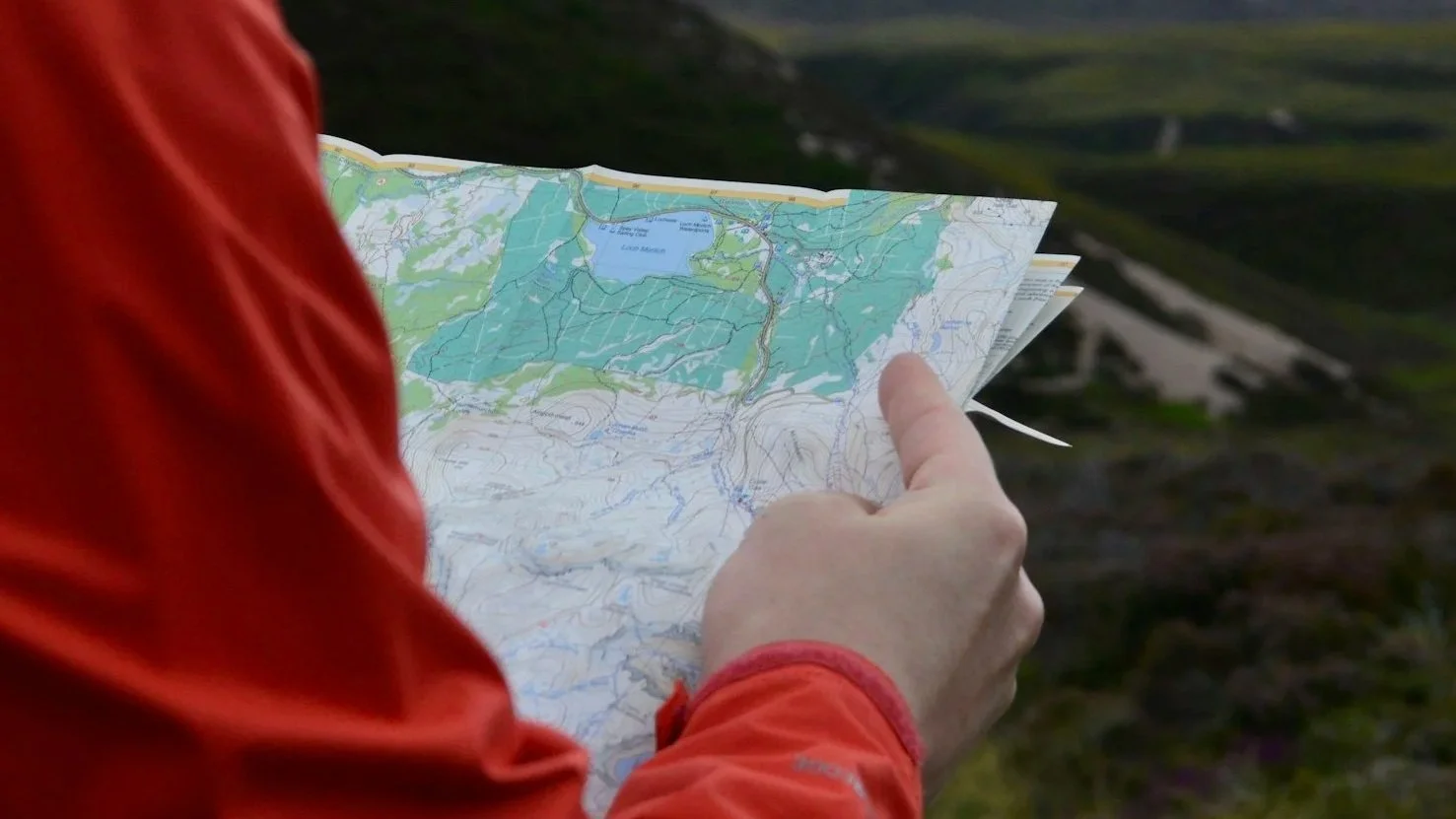 Hiker in a red jacket pointing at a topographic map outdoors