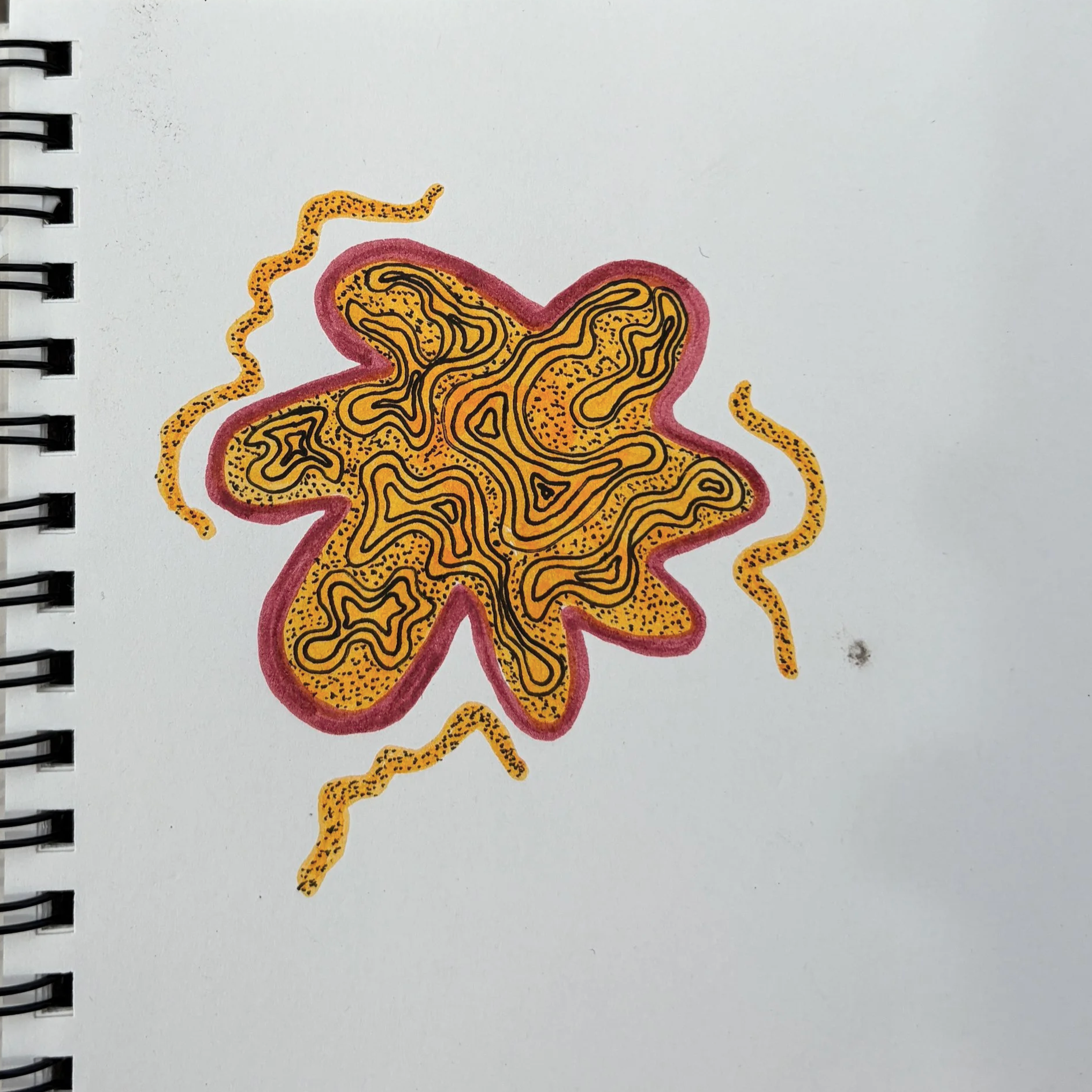 A colorful star-shaped sticker with black and yellow swirling patterns, outlined in red, with yellow extensions around it, placed on a white paper notebook page.