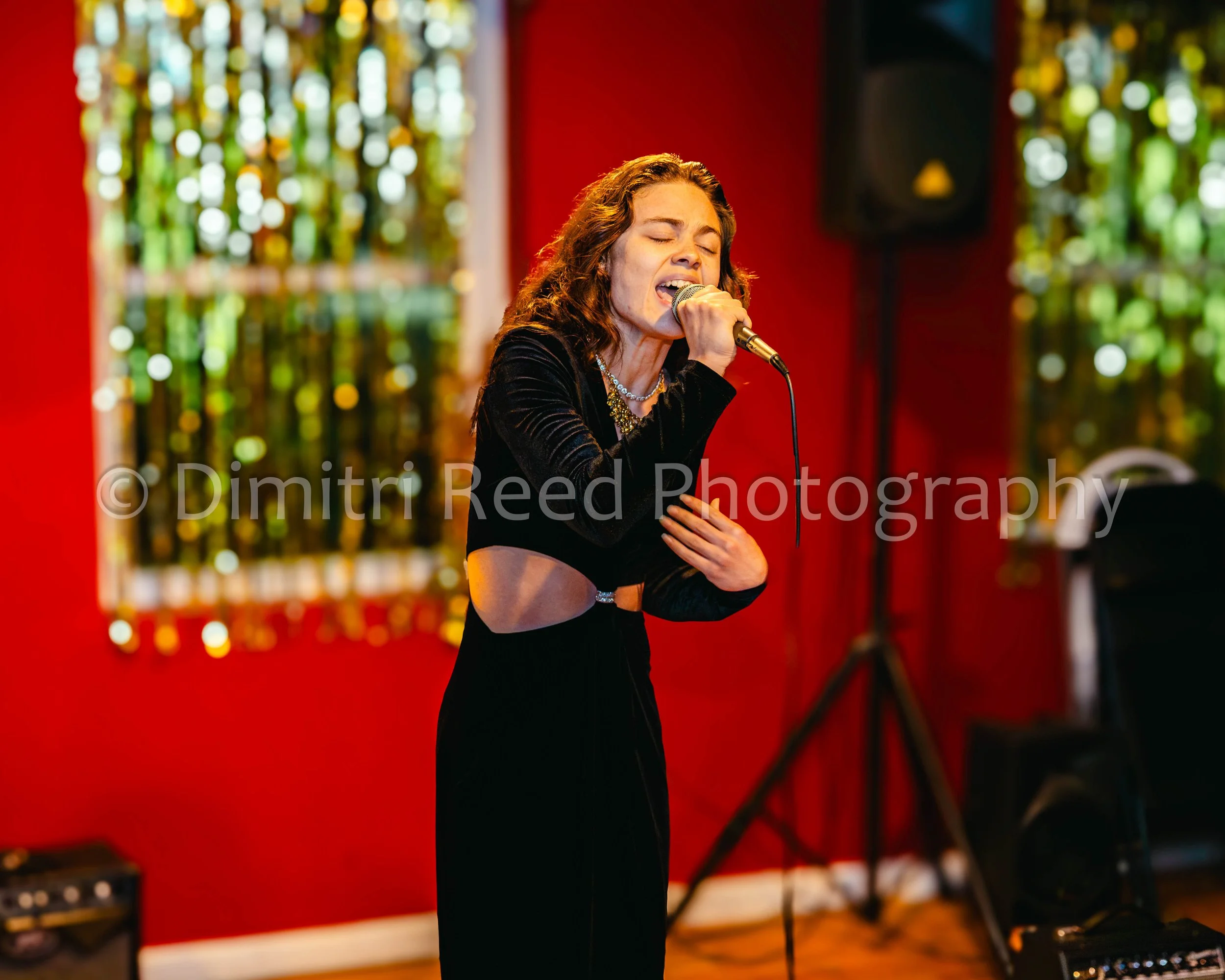 A woman singing into a microphone in a red room with colorful blurred background.