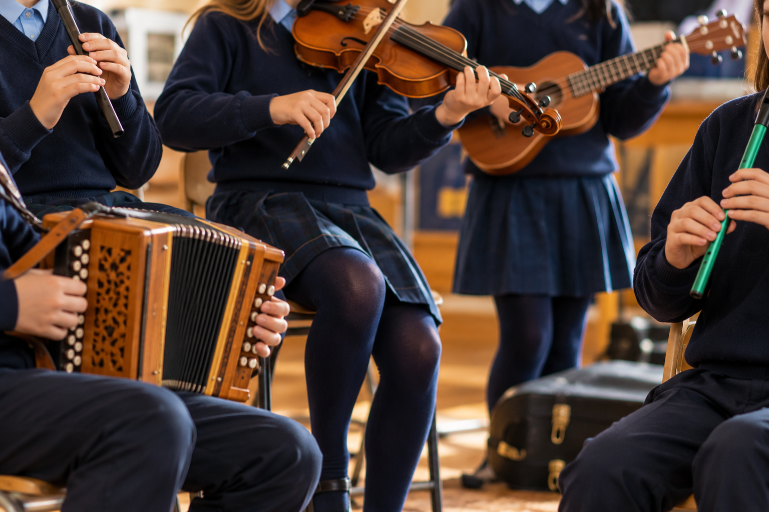Children playing musical instruments in a school classroom, including a violin, flute, accordion, and ukulele.