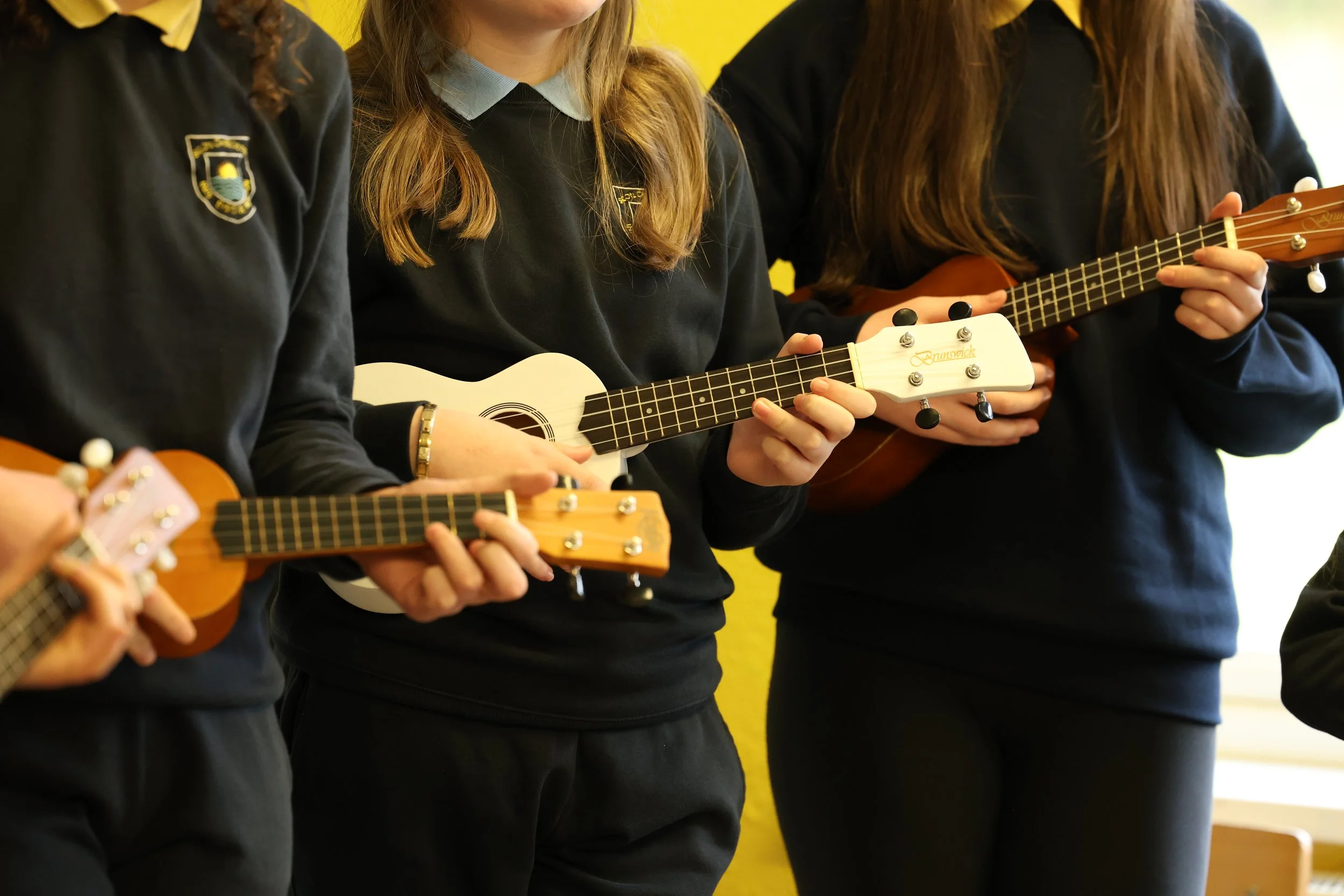 A group of students wearing school uniforms playing ukuleles during a music class.