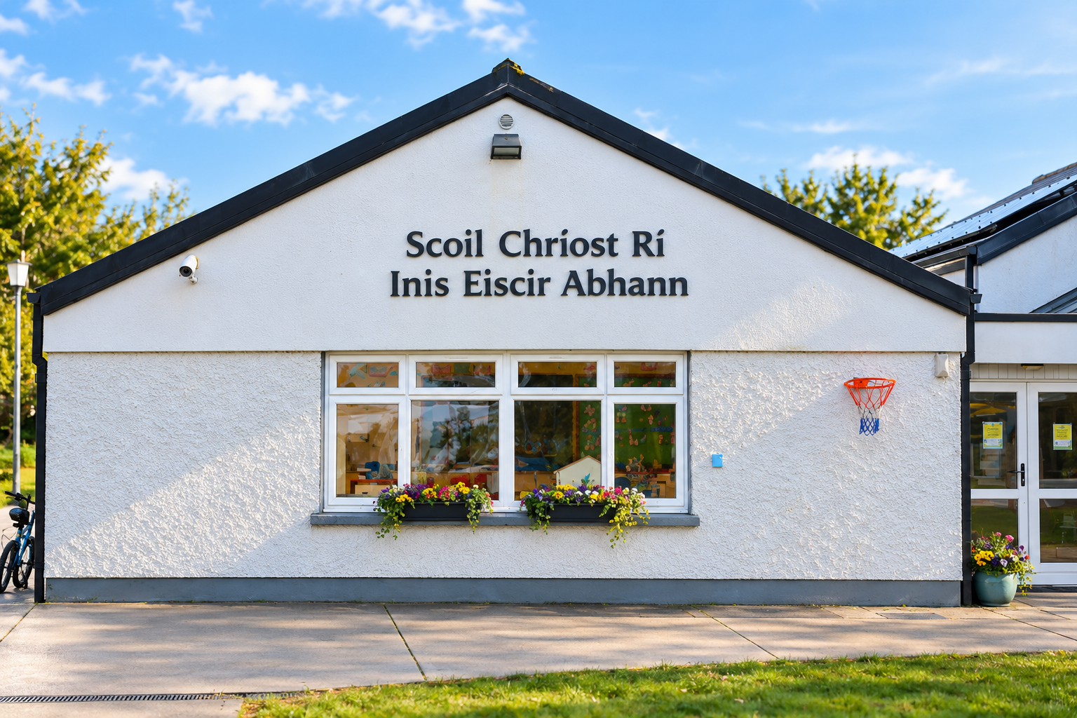 White building with black roof, large window with flowers, and a small basketball hoop on the wall. The building has Irish text on the sign.