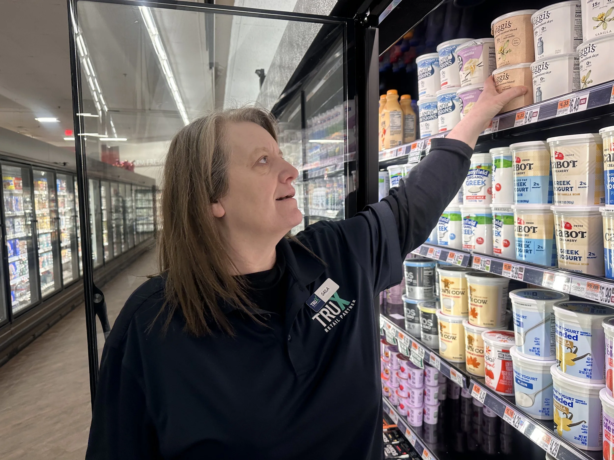 Woman selecting a Greek yogurt from the refrigerated shelves in a grocery store.