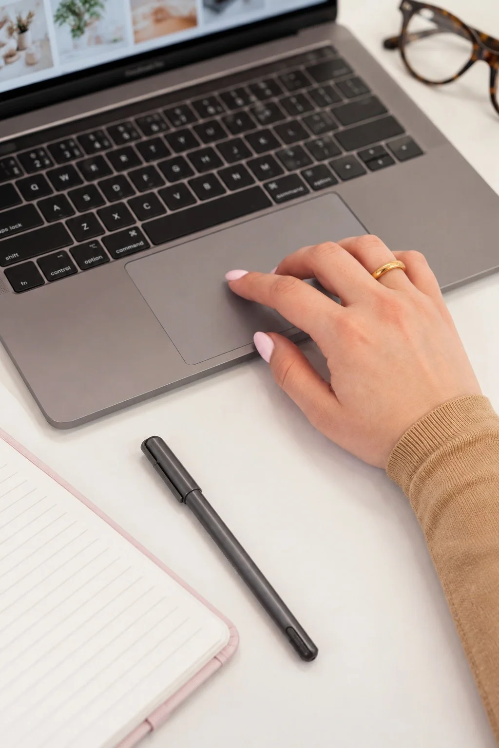 A hand resting on a laptop trackpad beside a notebook and pen.