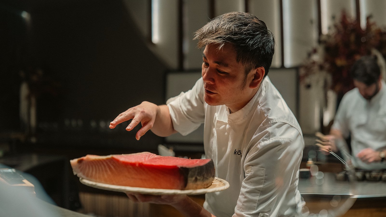 Chef presenting a large raw fish steak in a professional kitchen.