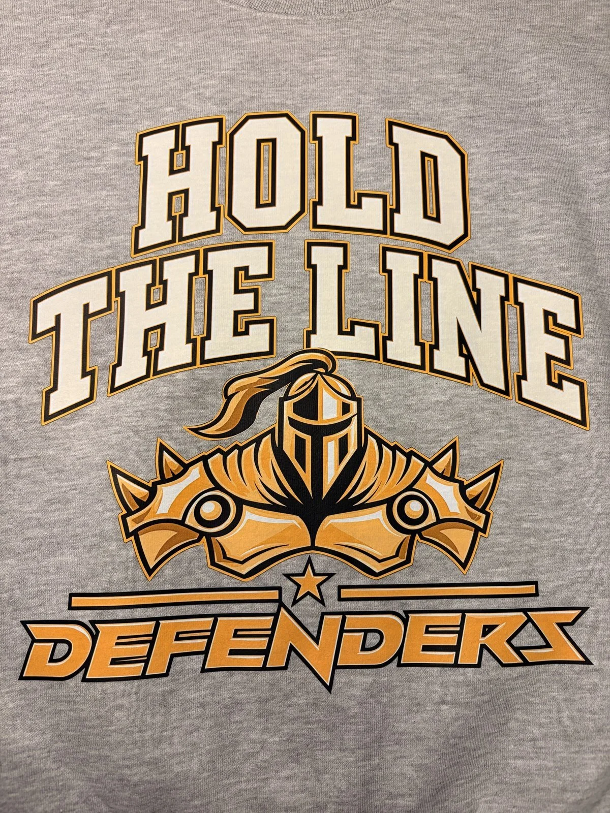  Heather gray shirt printed with Hold the Line over a gold armor helmet and Defenders wordmark