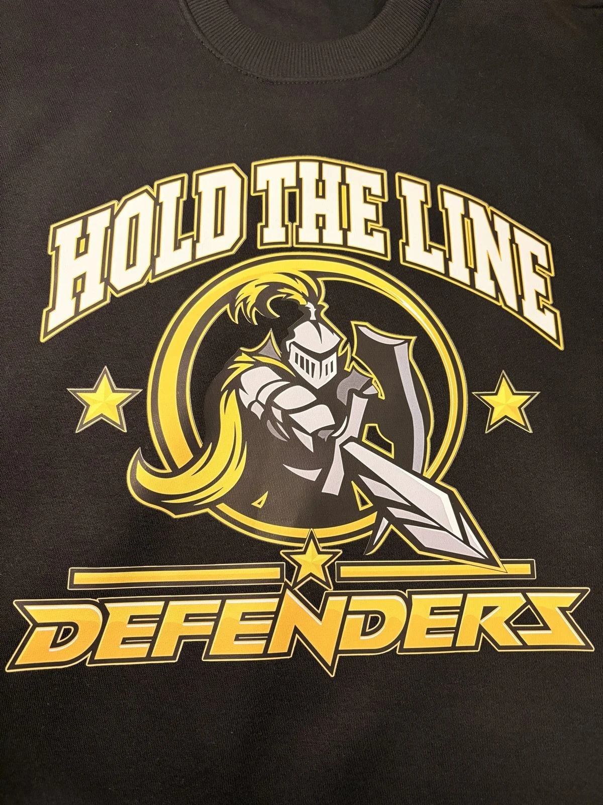 Black sweatshirt printed with Hold the Line, a knight with sword and the Defenders wordmark