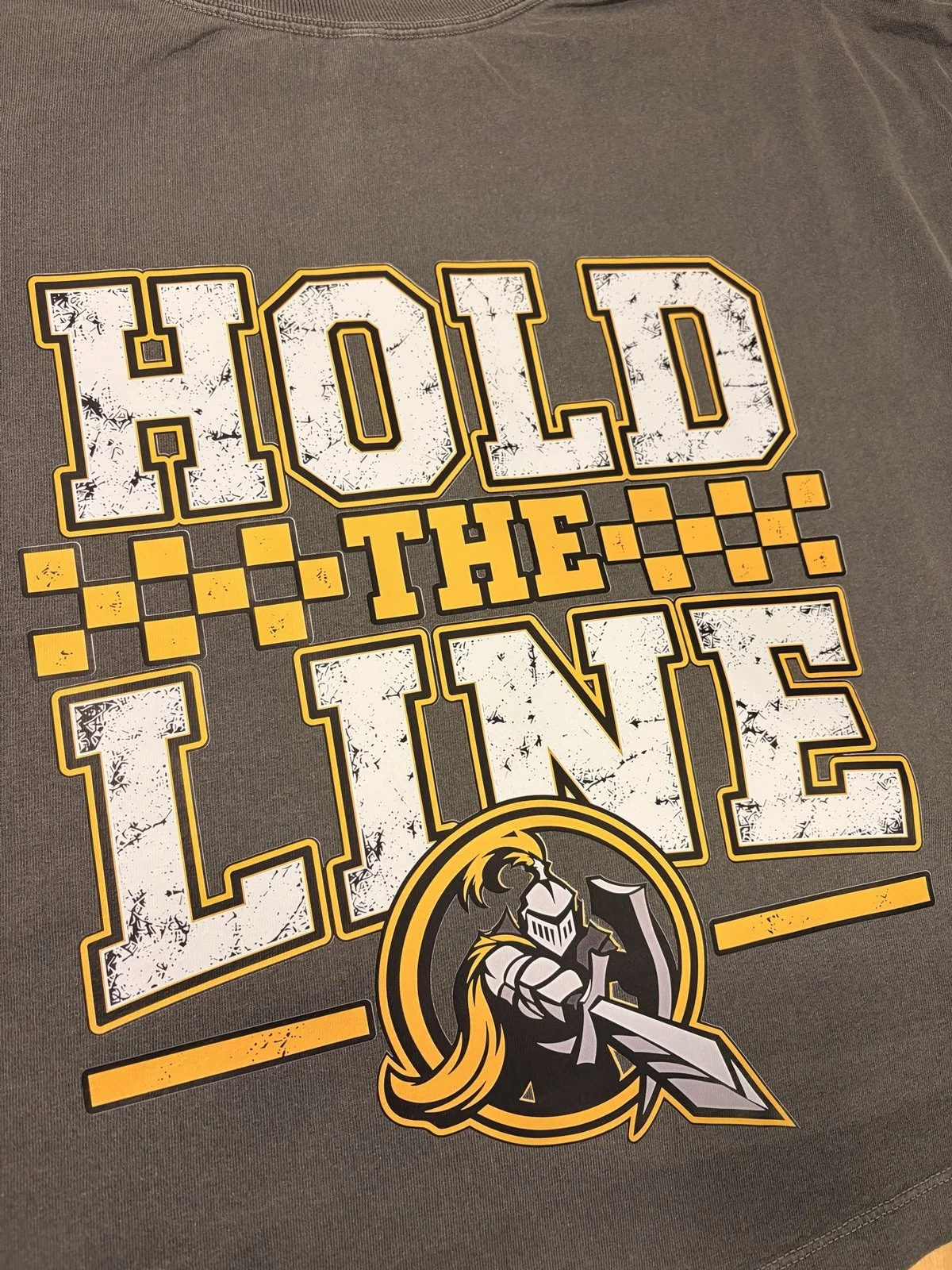 Charcoal shirt printed with a distressed Hold the Line checkerboard design with a knight logo