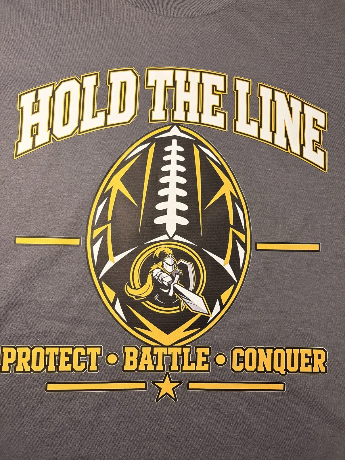 Gray shirt printed with a Hold the Line football and knight design that reads Protect Battle Conquer