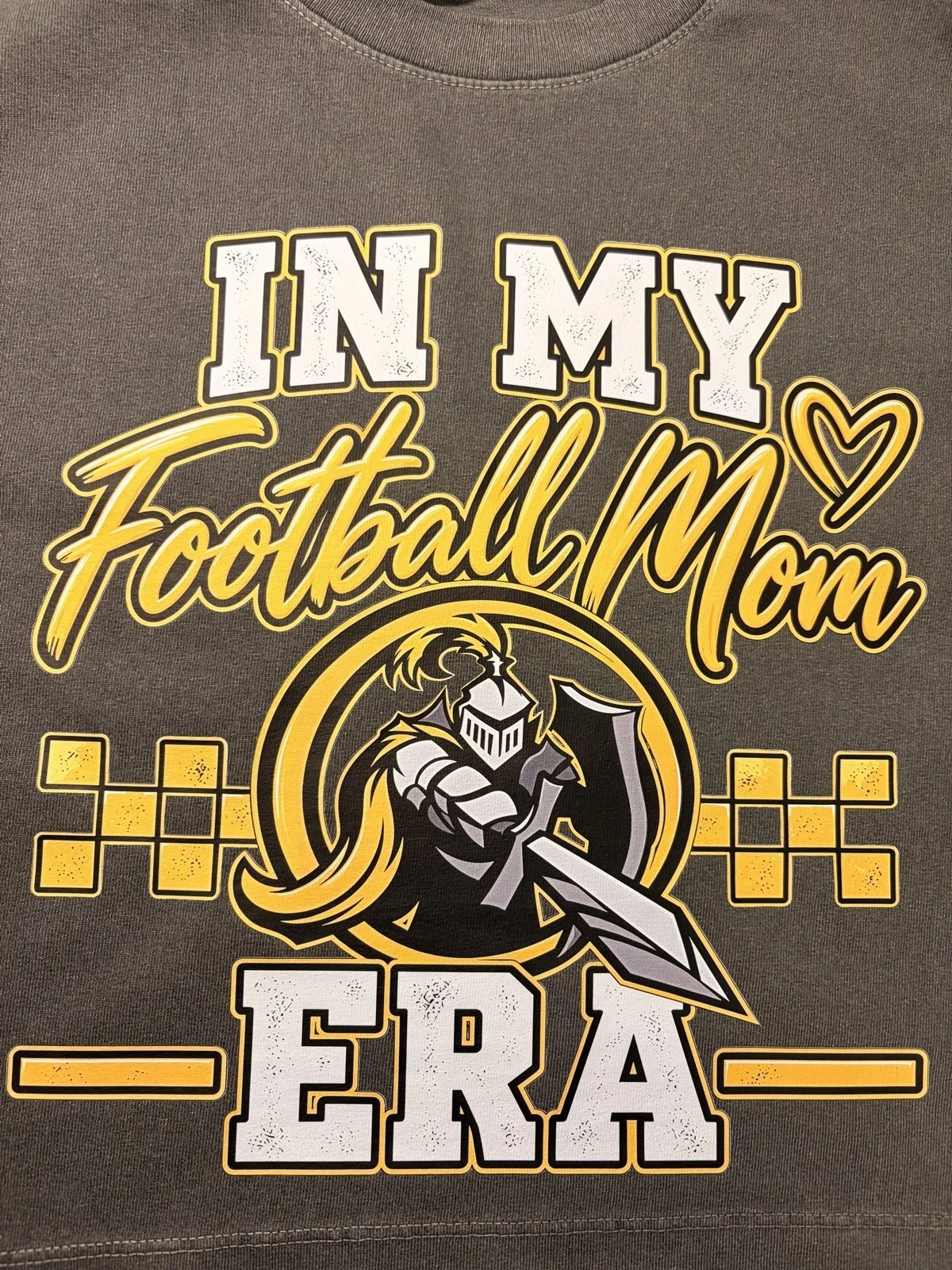 Charcoal shirt printed with an In My Football Mom Era design with a knight and checkerboard in gold