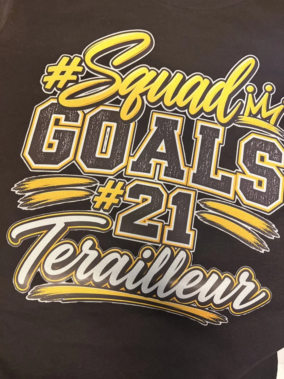 Black shirt printed with a Squad Goals #21 script and varsity lettering design in gold