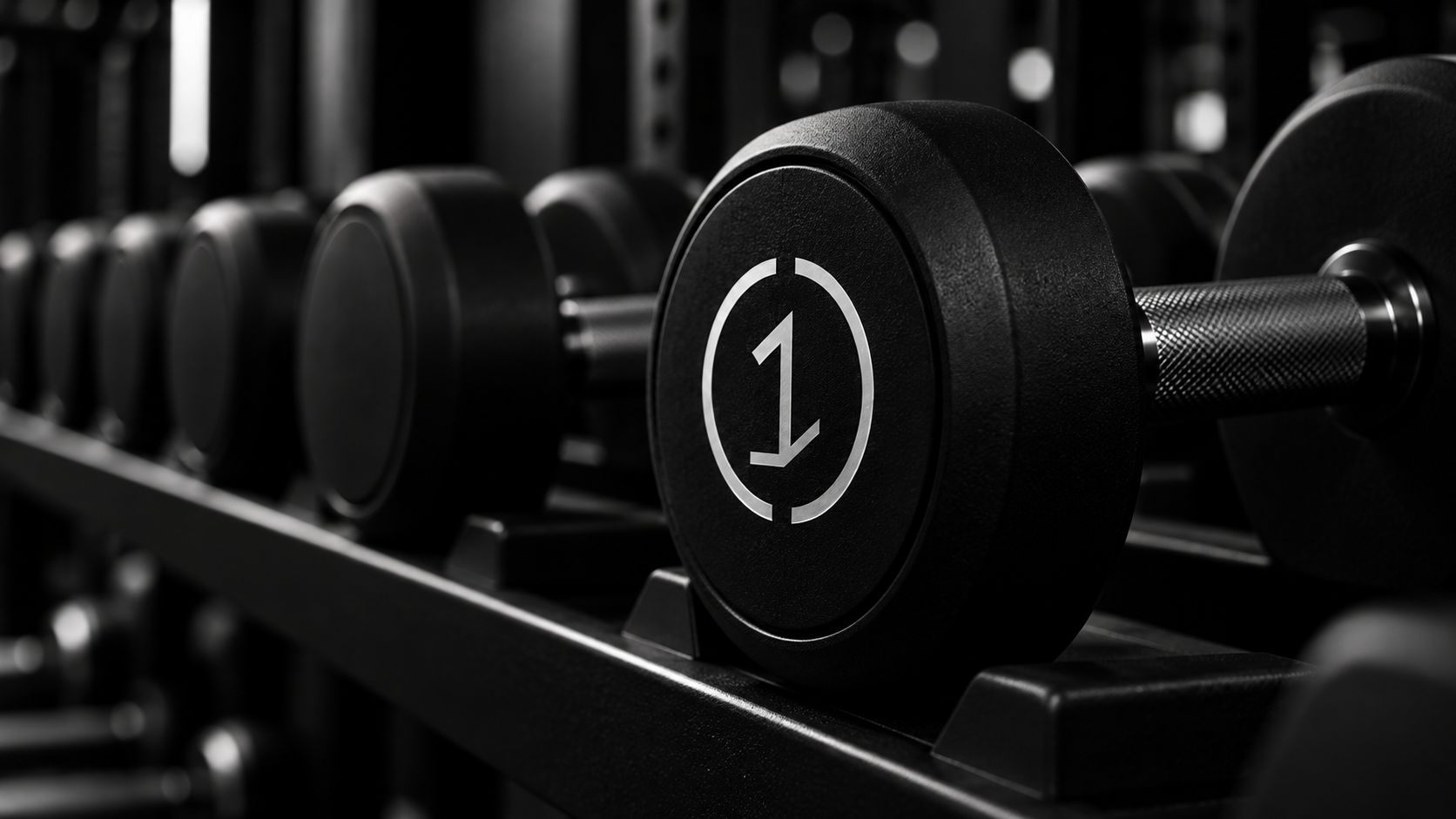 Close-up of a black dumbbell with the number 1 on the weight, arranged on a rack in a gym. The background is dark and blurred.