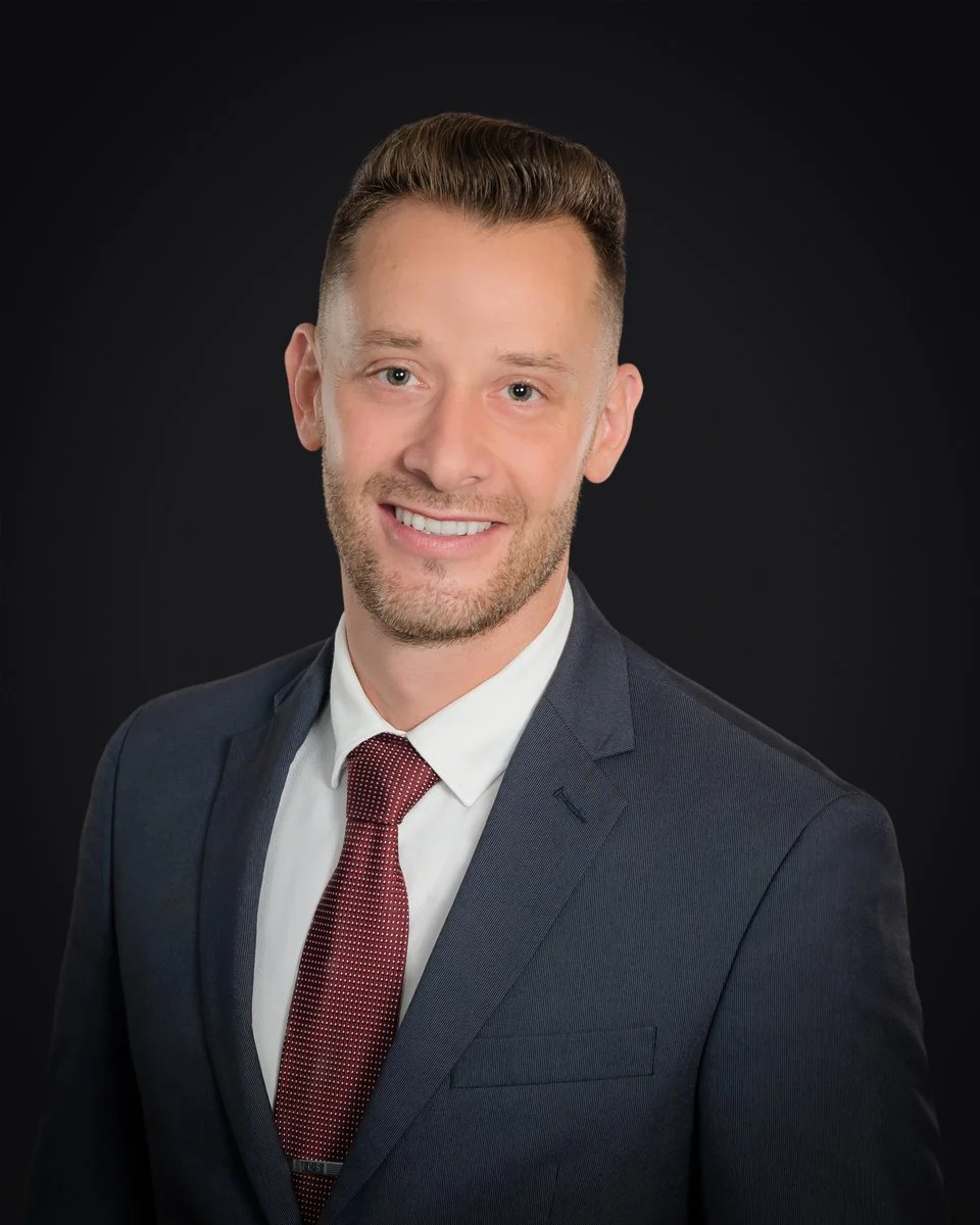 Executive headshot of a businessman in a navy suit and burgundy tie on a dark studio background