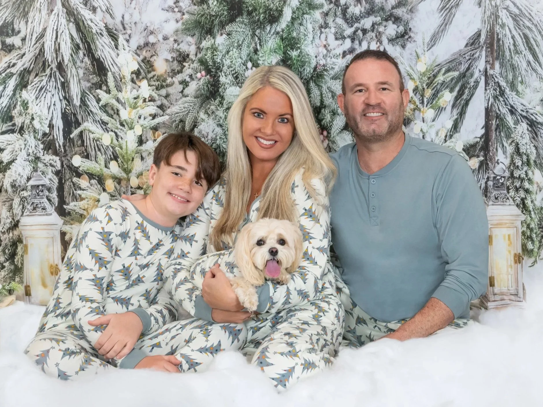 Family holiday portrait in matching pajamas with their small dog in a snowy winter studio set, Christmas photos by Vasi Studio