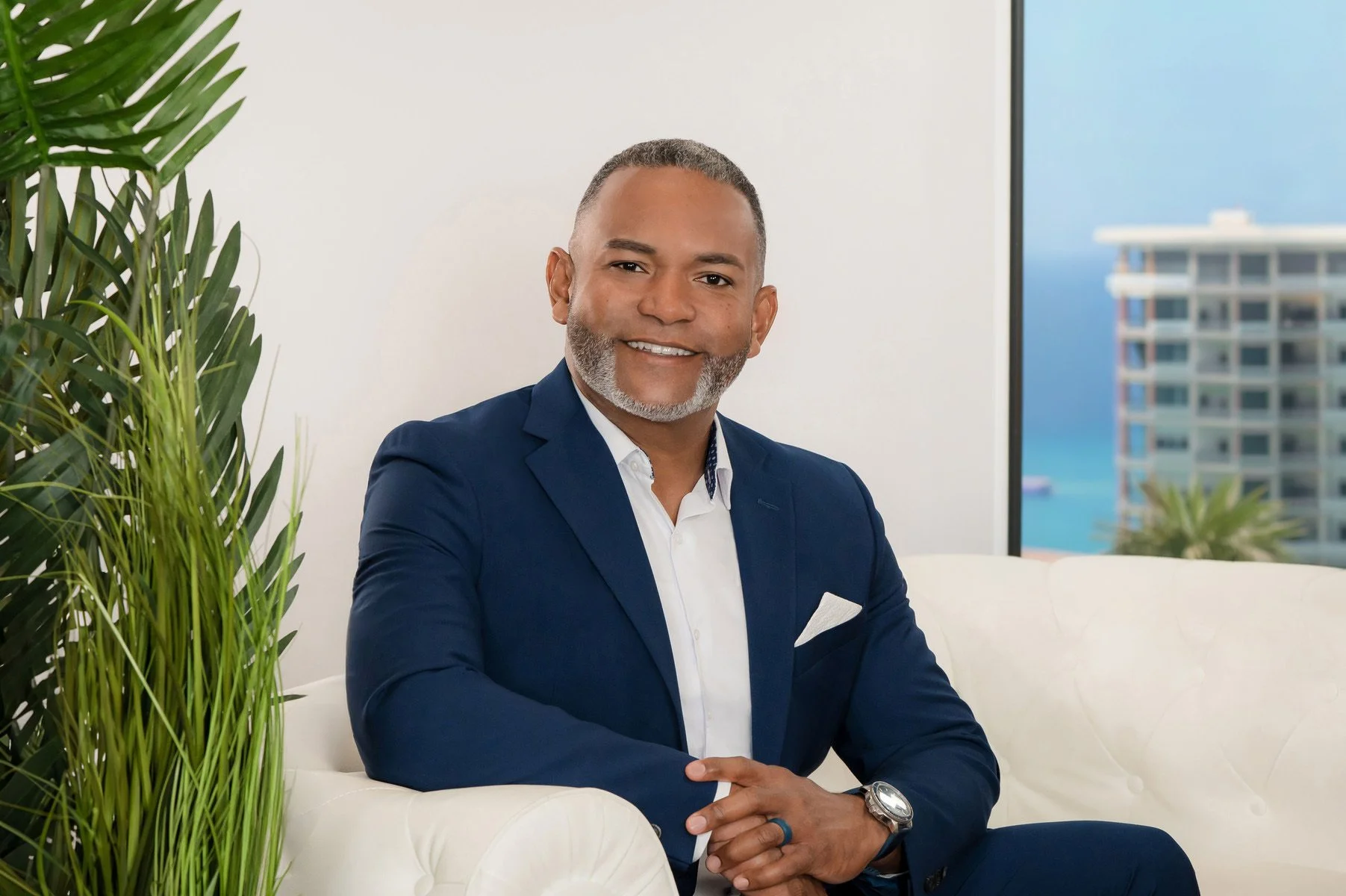 Executive in a navy suit seated in a bright office with an ocean view, professional headshot by Vasi Studio in Palm Beach
