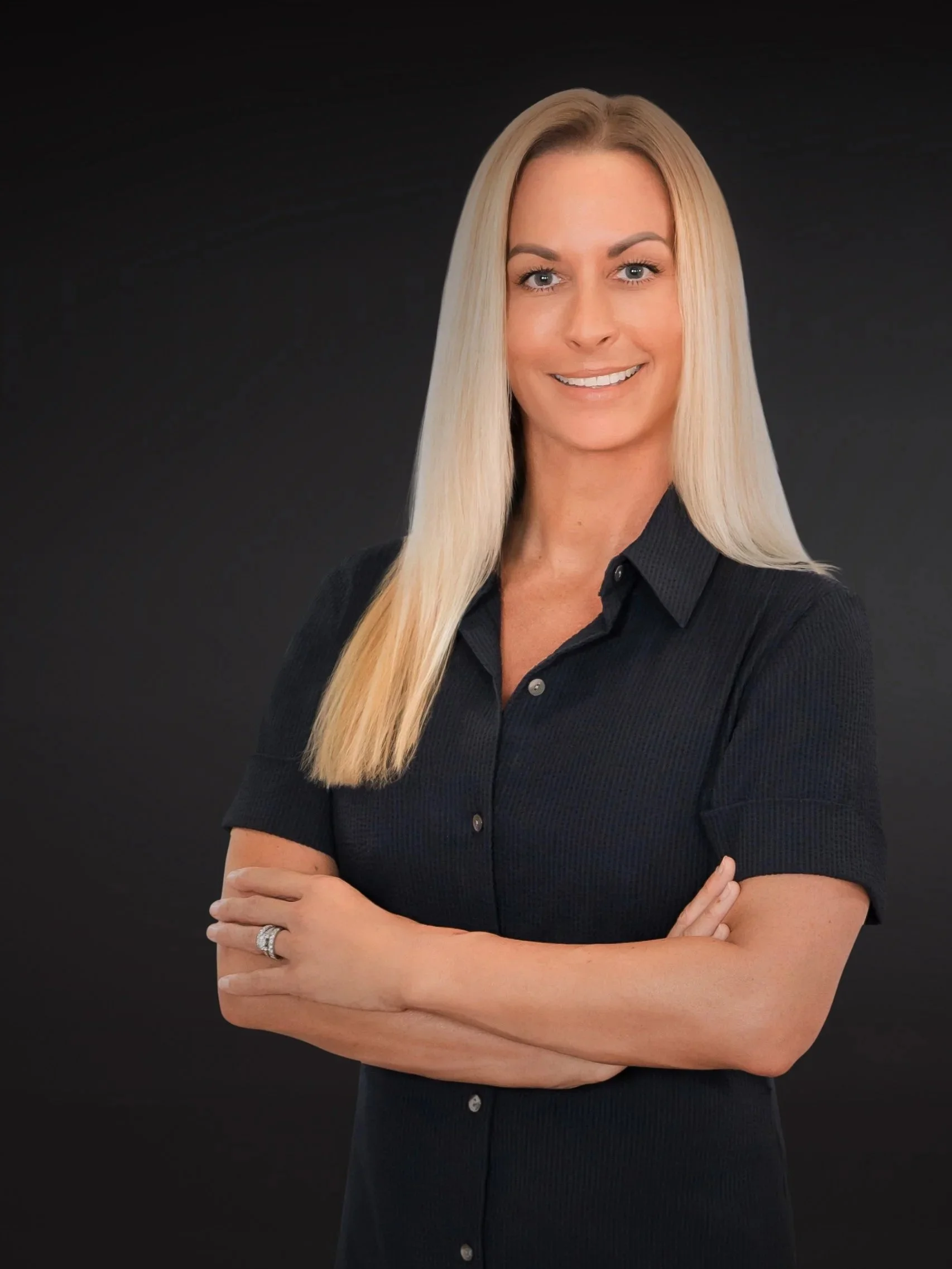 Modern personal branding portrait of a woman in black with arms crossed on a dark studio background