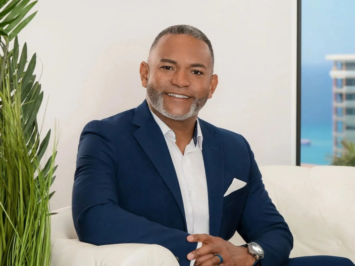 Executive portrait of a businessman in a navy suit seated in a bright ocean-view office, modern CEO portrait