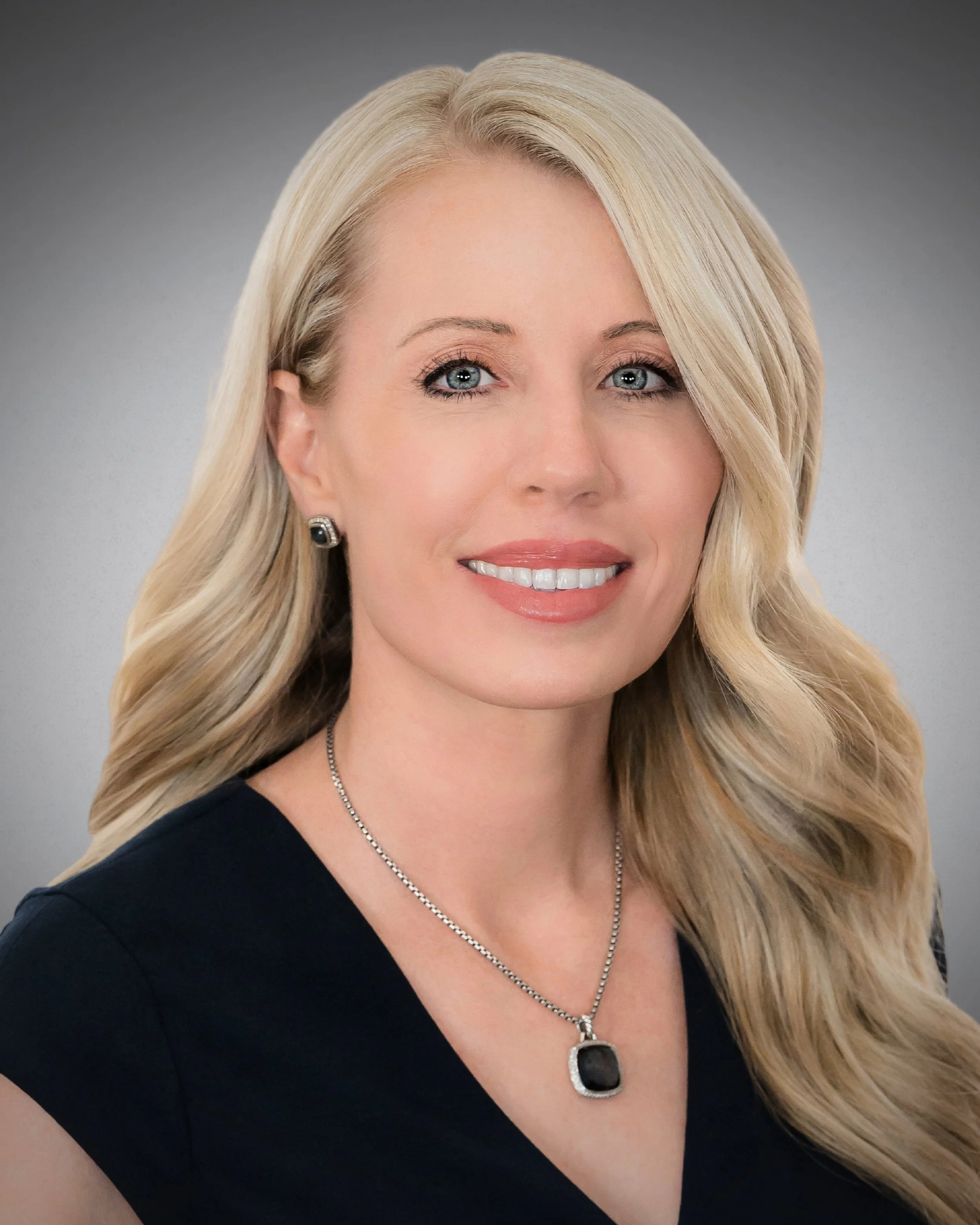 Classic professional headshot of a smiling blonde businesswoman on a gray studio background, Palm Beach Gardens headshots
