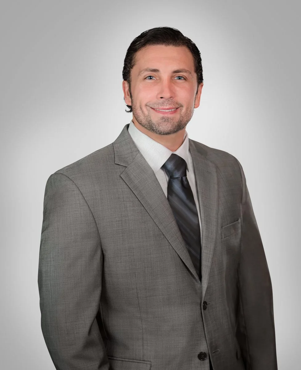 Corporate headshot of a businessman in a gray suit and tie on a gray studio background
