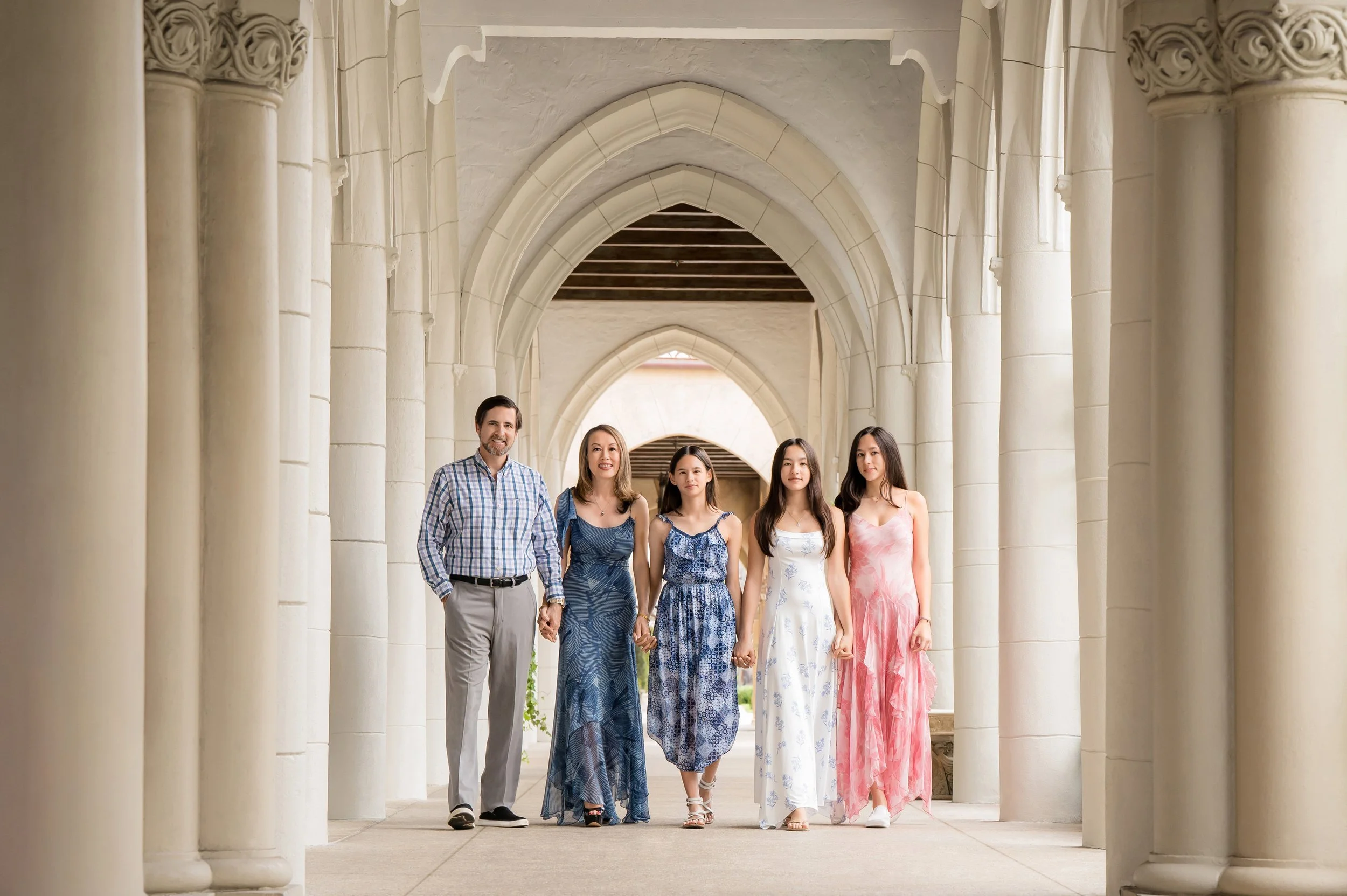 Family portrait of five walking hand in hand through a white arched colonnade, Palm Beach family photographer Vasi Studio