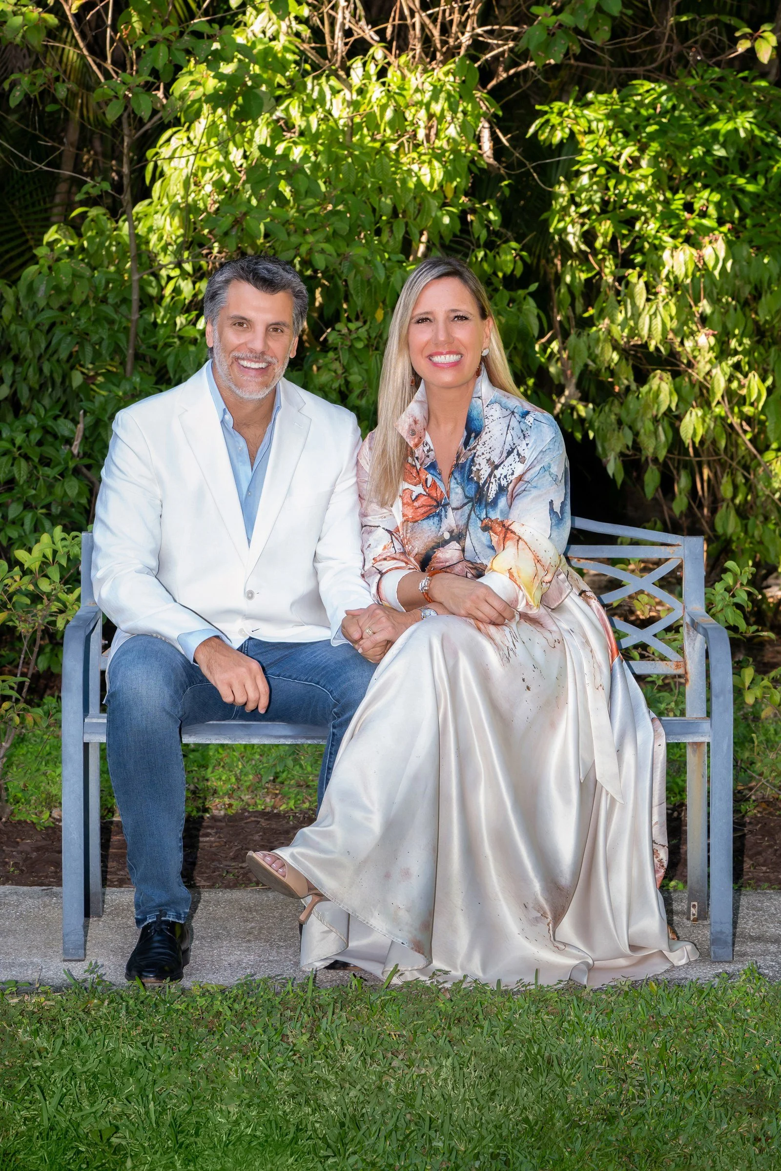 Couple seated on a garden bench in elegant attire among lush greenery, couples portrait Palm Beach Gardens