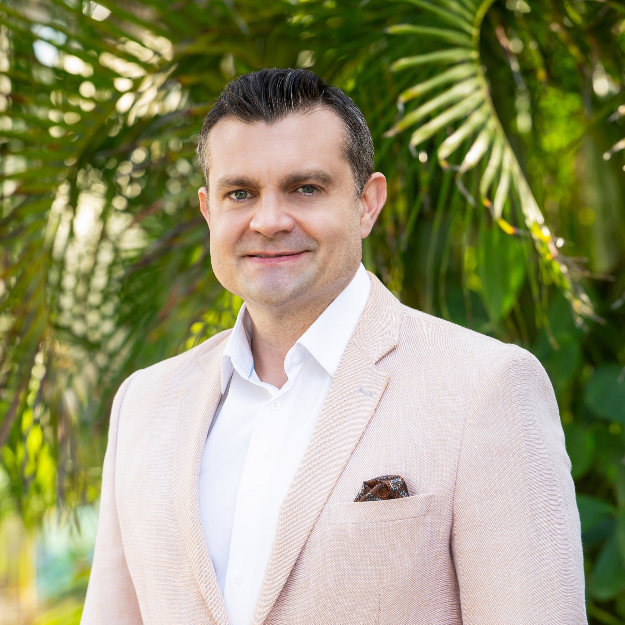 Business casual portrait of a man in a cream blazer among palm fronds, outdoor branding photography Florida