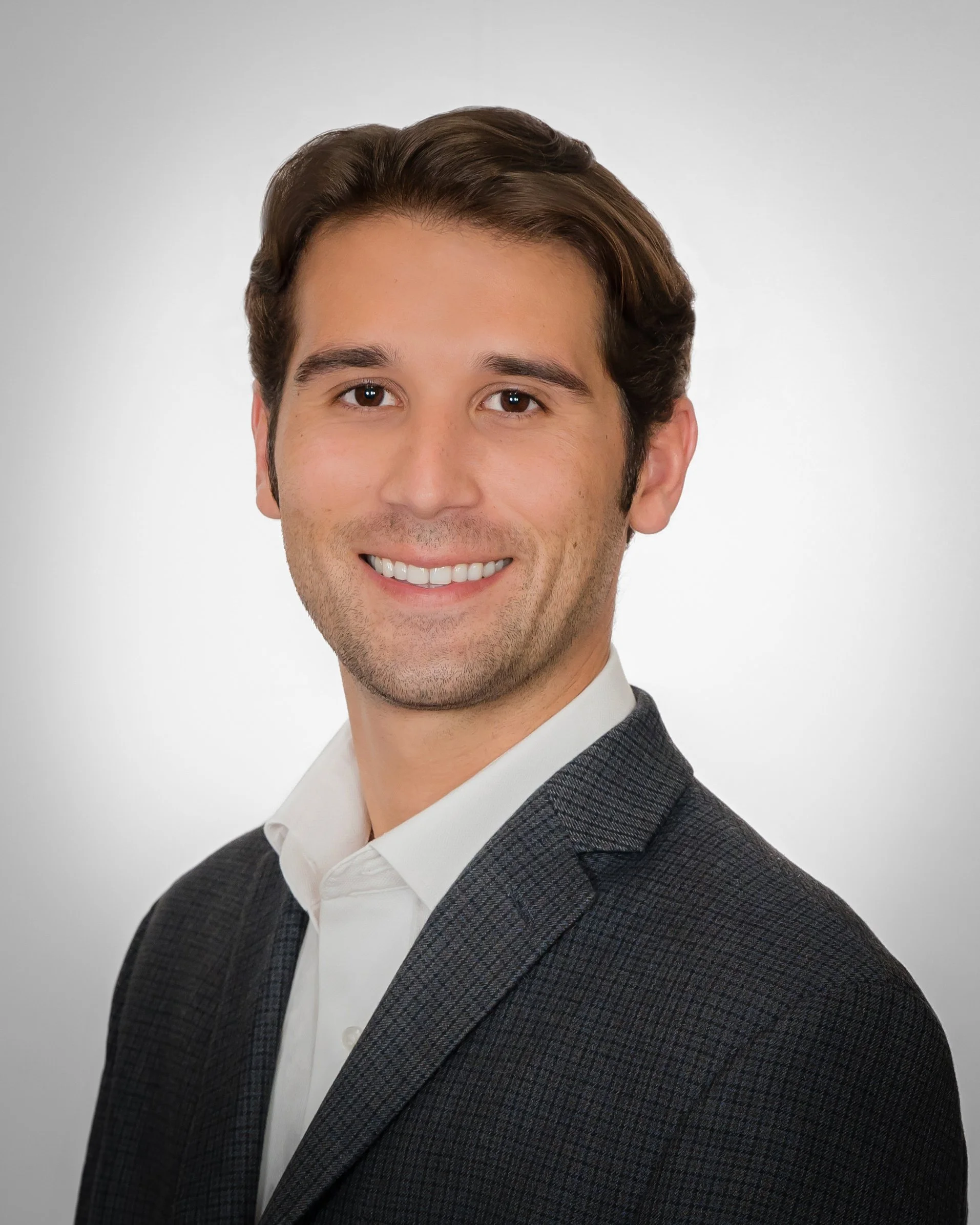 LinkedIn headshot of a smiling young professional man in a dark blazer on a light gray background