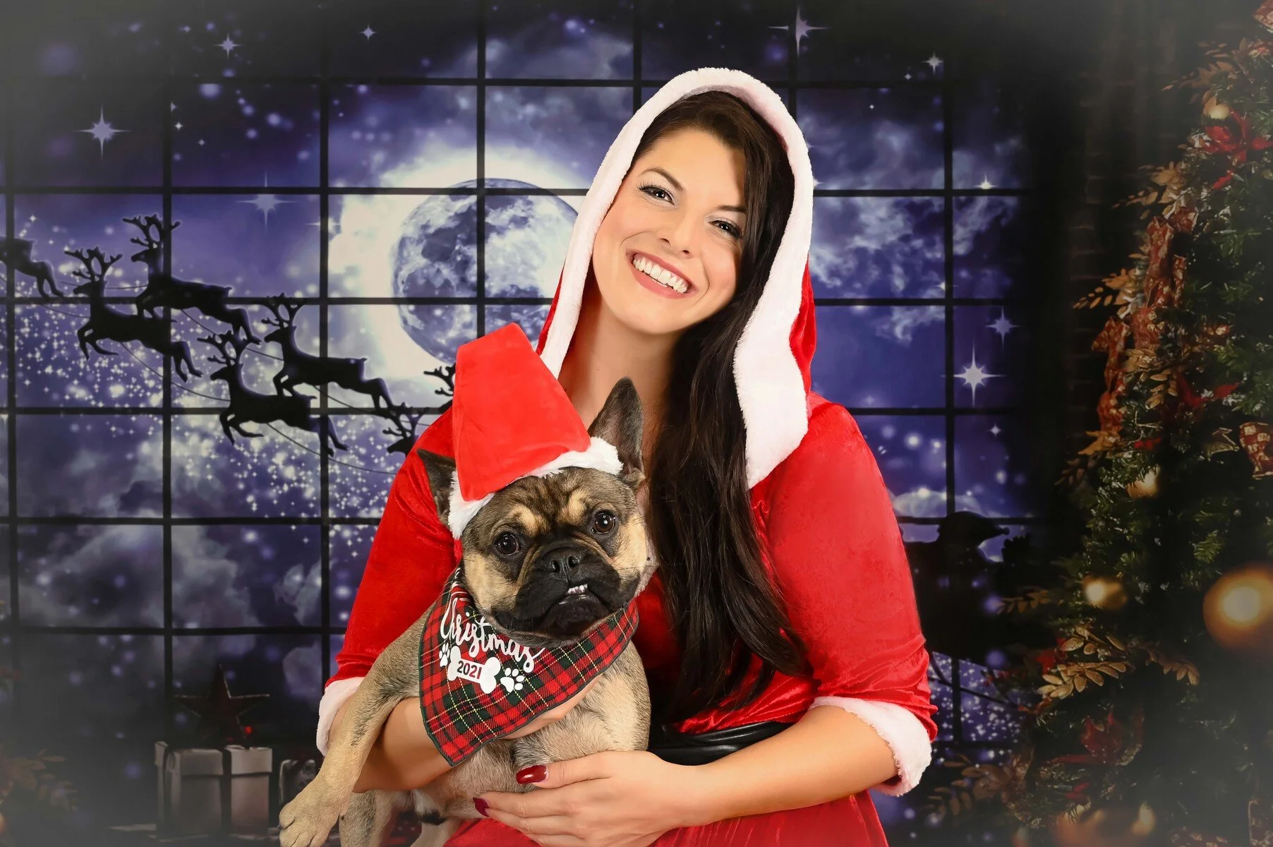 Woman in a red hooded cape holding a pug under a moonlit Santa sleigh sky, creative Christmas pet portrait