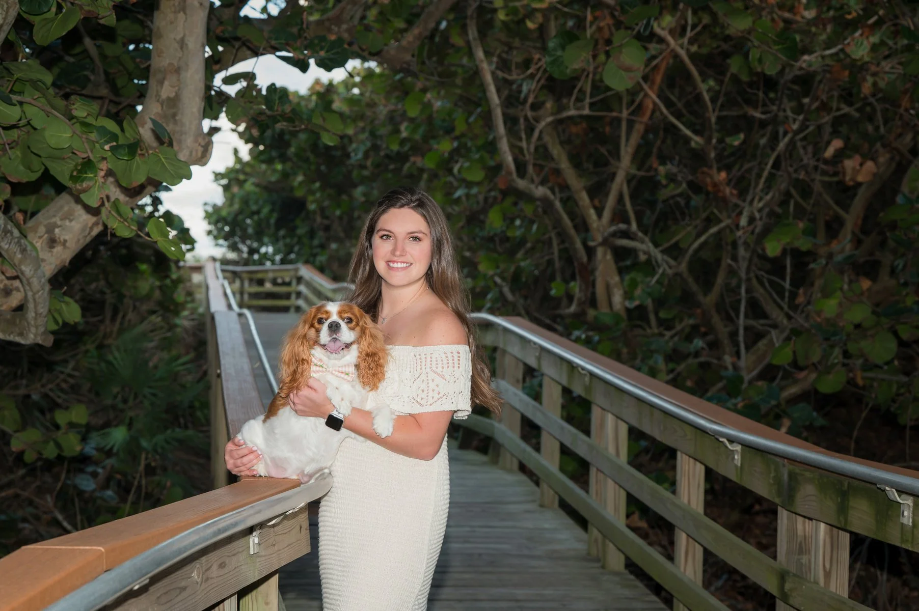 Young woman holding her small dog on a wooden boardwalk in a coastal hammock, outdoor portrait Jupiter area