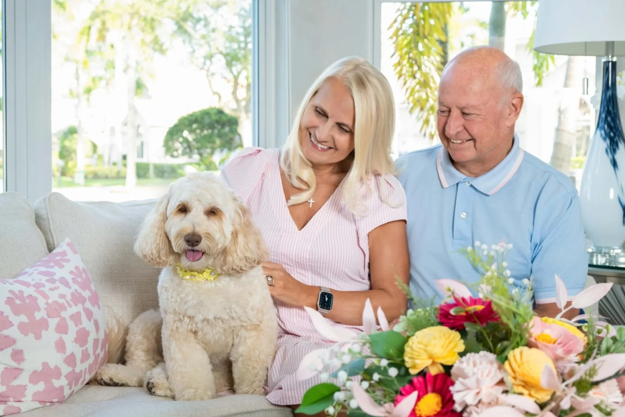 Couple at home with their goldendoodle and flowers in a bright living room, in-home family and pet portrait