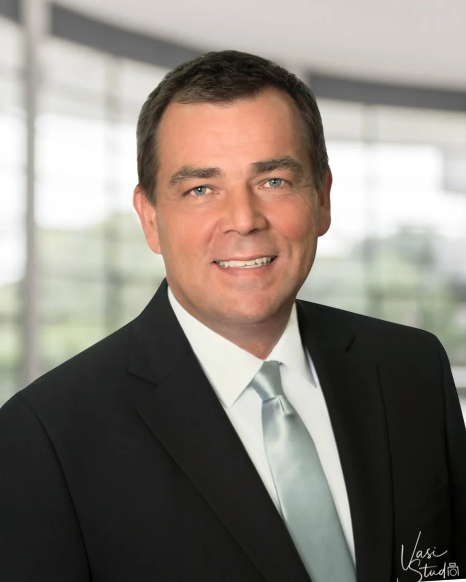 Corporate executive headshot of a businessman in a dark suit in a modern office, Vasi Studio