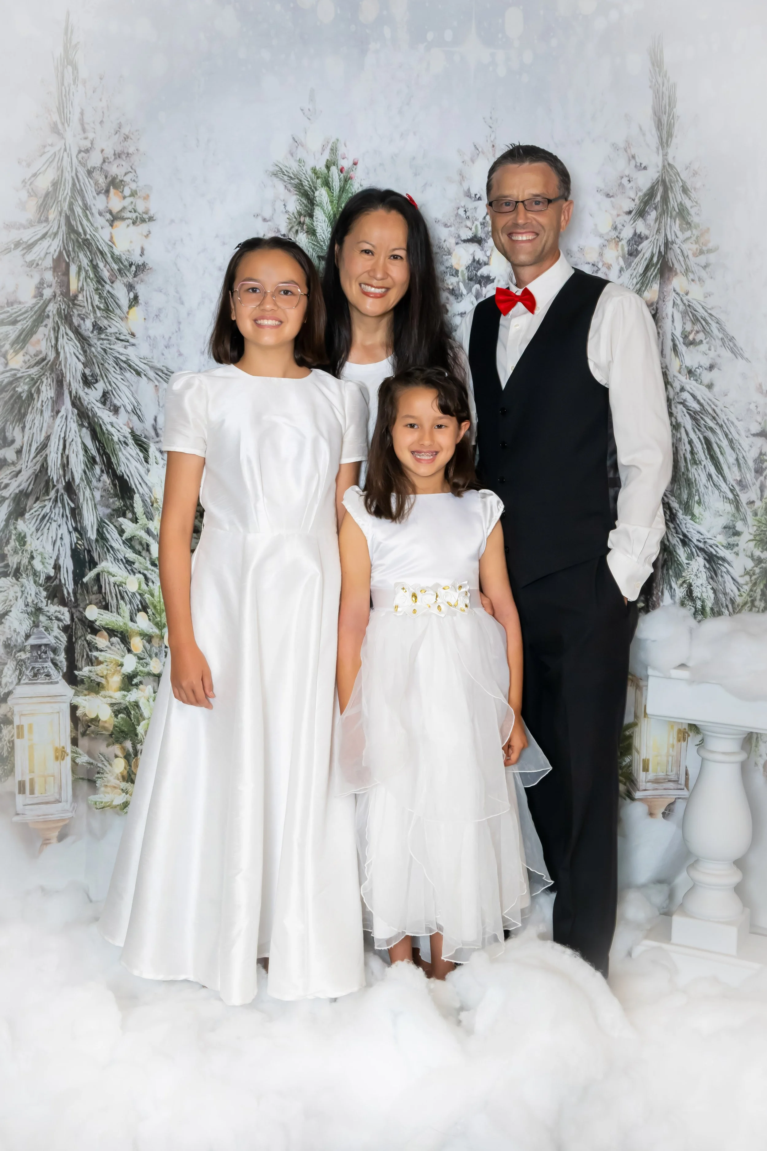 Family holiday portrait in white dresses and a black vest in a snowy winter wonderland studio set, indoor Christmas photography by Vasi Studio in Palm Beach Gardens