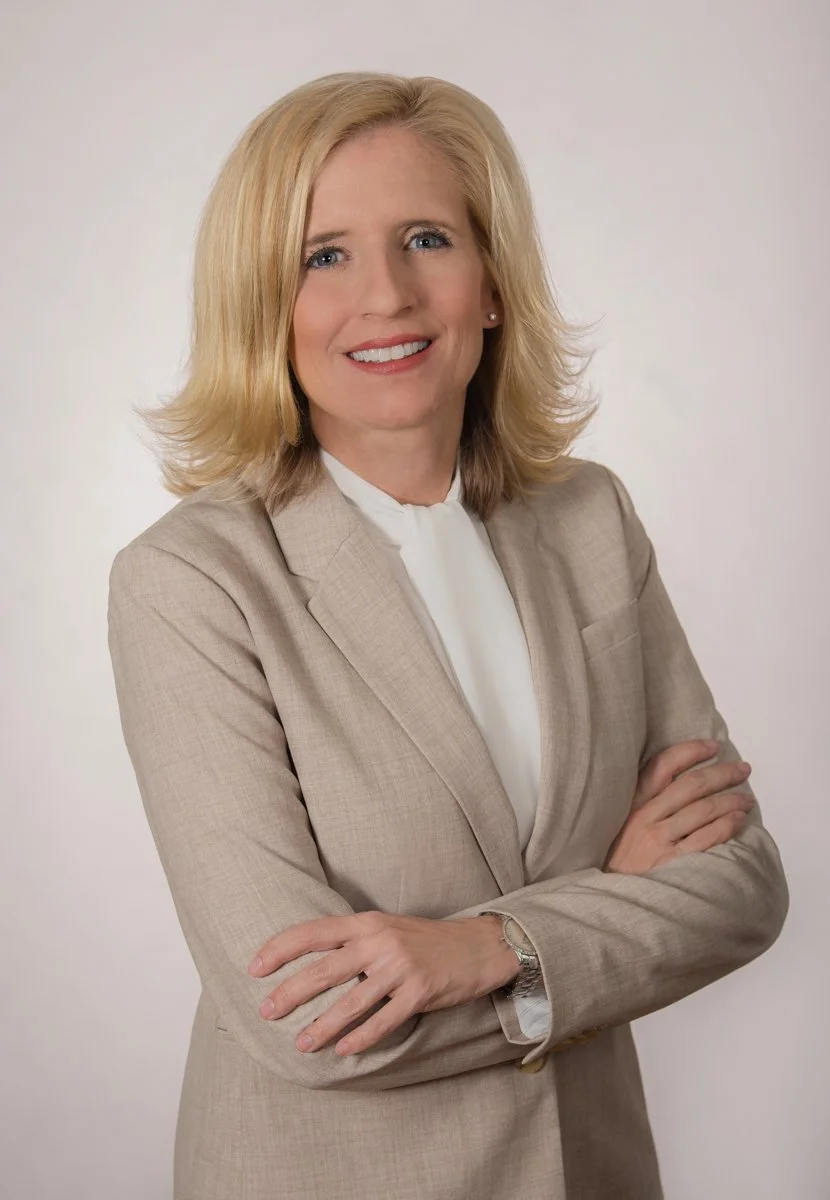 Confident business portrait of a woman in a beige blazer with arms crossed on a light studio background