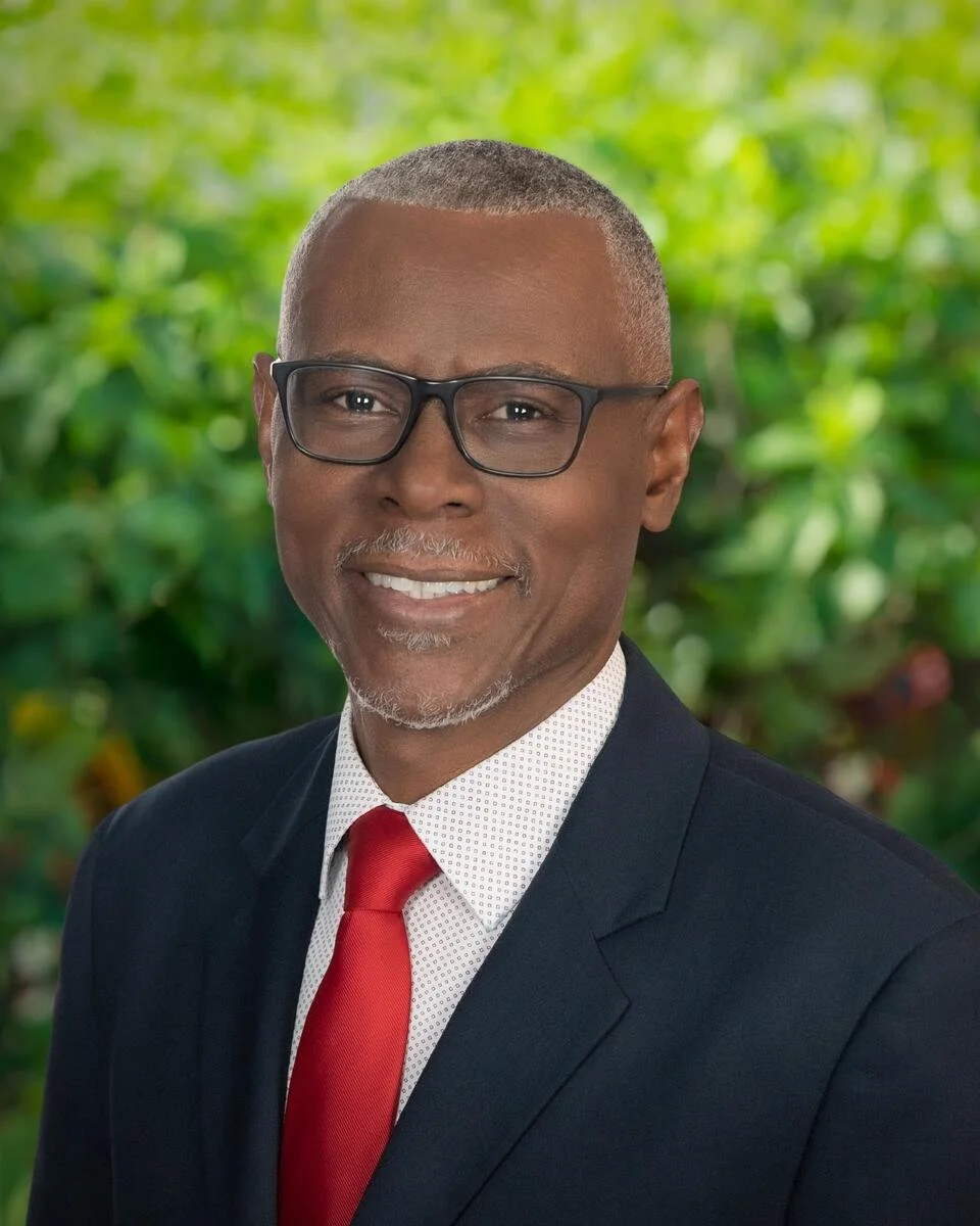 Executive portrait of a businessman in glasses, navy suit and red tie against tropical greenery