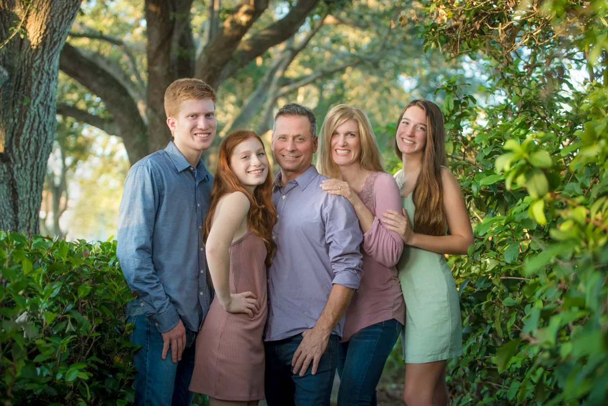 Family of four standing together in a lush tropical garden, family portrait by Vasi Studio in Palm Beach Gardens