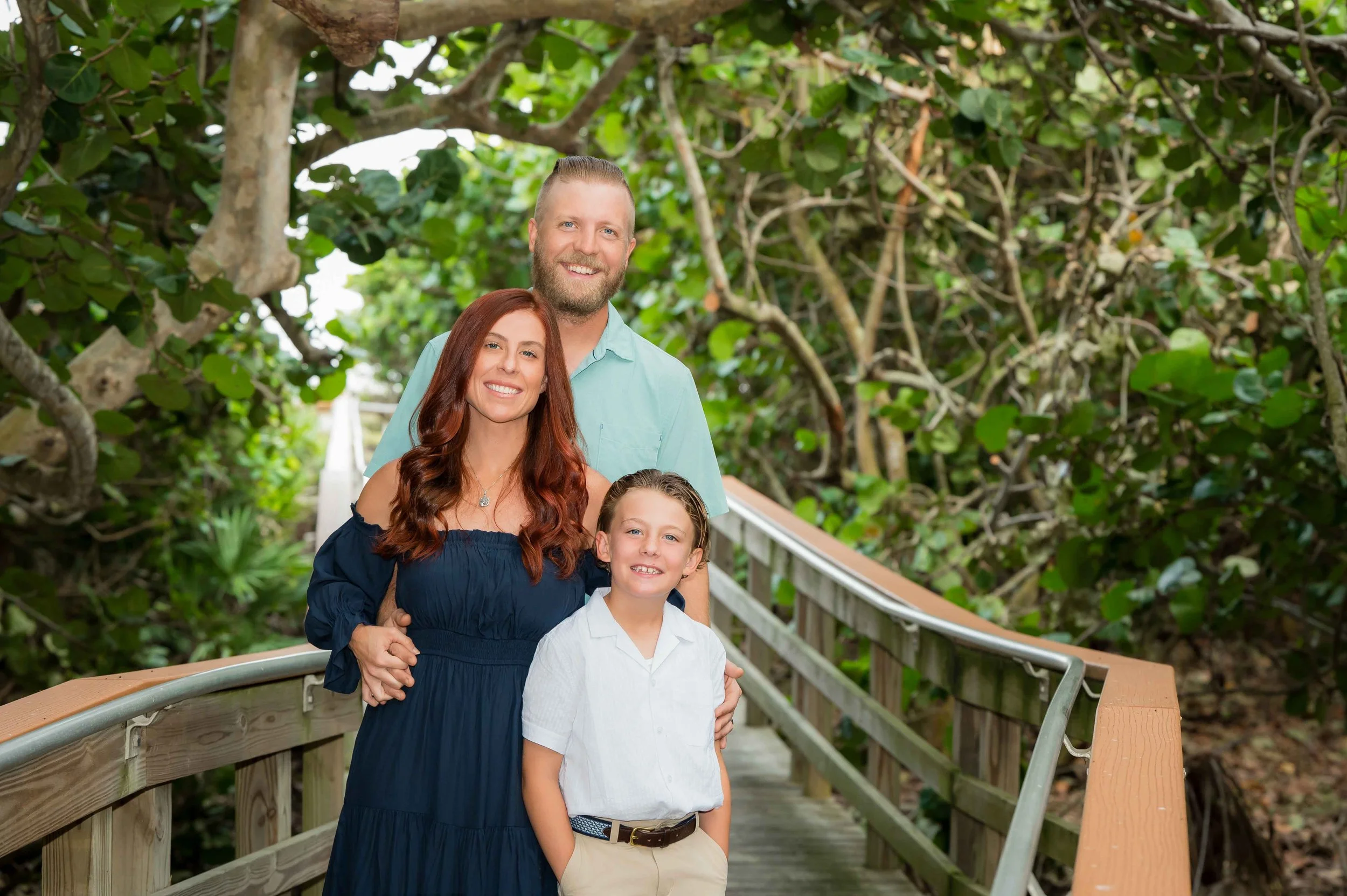 Mother, father and son on a boardwalk under a tropical canopy, outdoor family portrait in Jupiter area