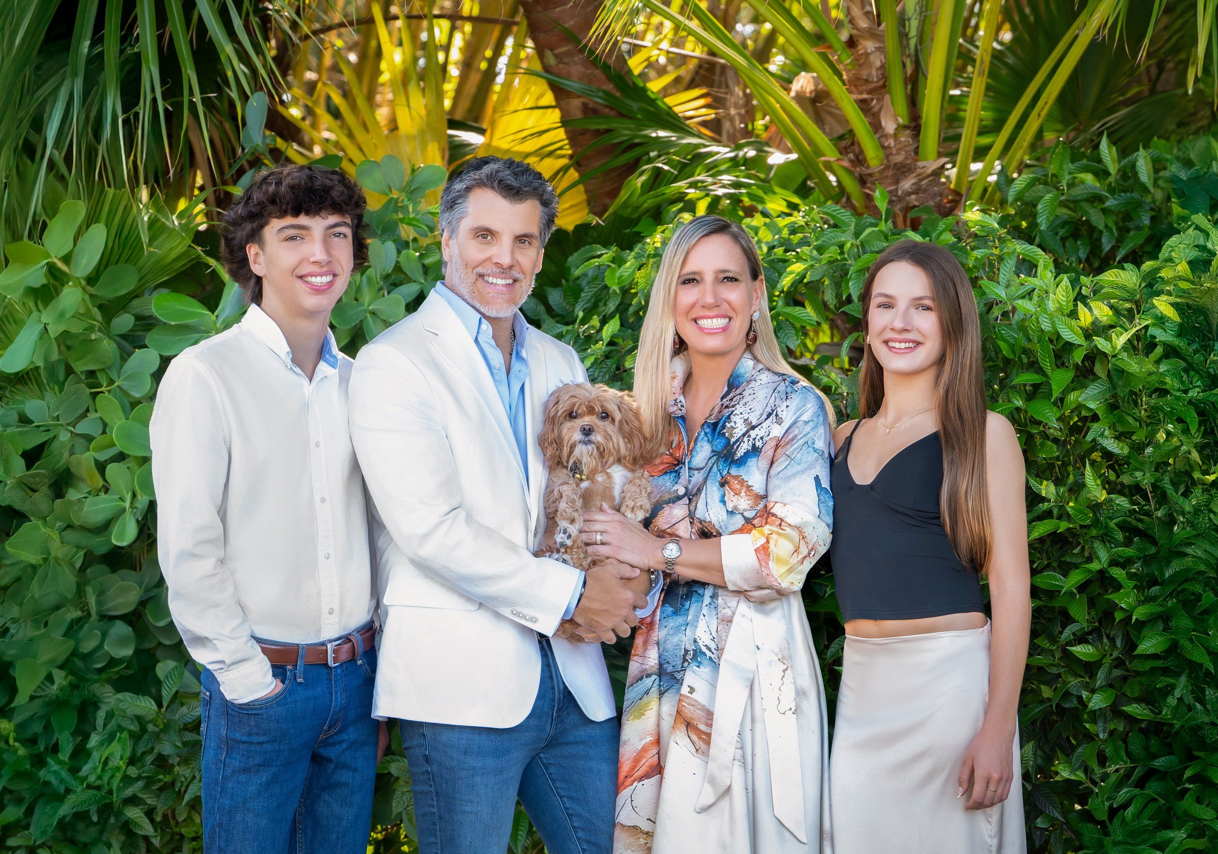 Family portrait with teens and their small dog among lush tropical greenery, outdoor family photography Palm Beach Gardens