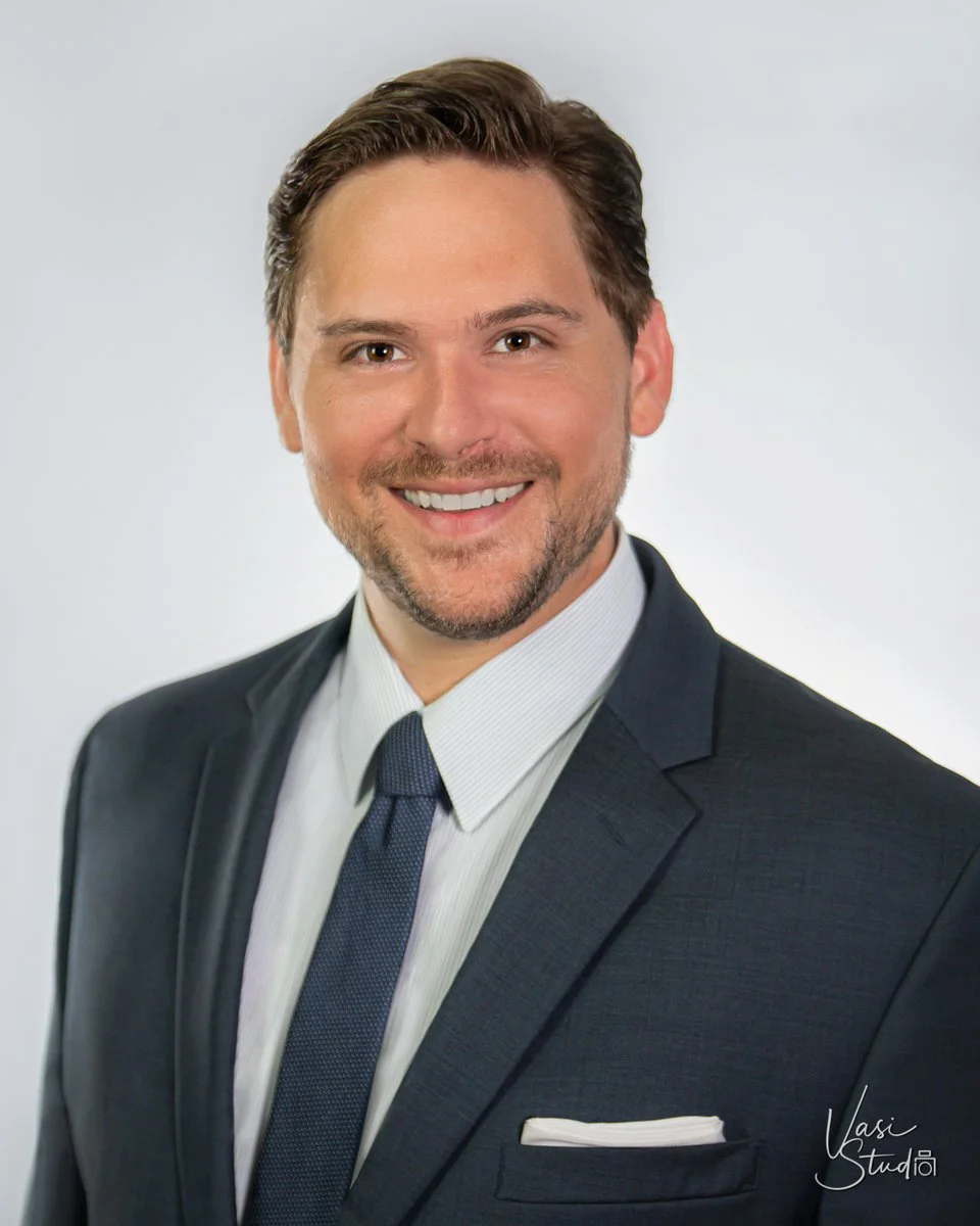 Corporate headshot of a smiling man in a navy suit and tie on a light gray background, Palm Beach Gardens headshot photographer