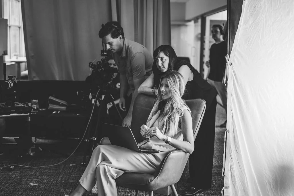 Women on film set, woman smiling with laptop, crew members around, camera equipment, indoor studio