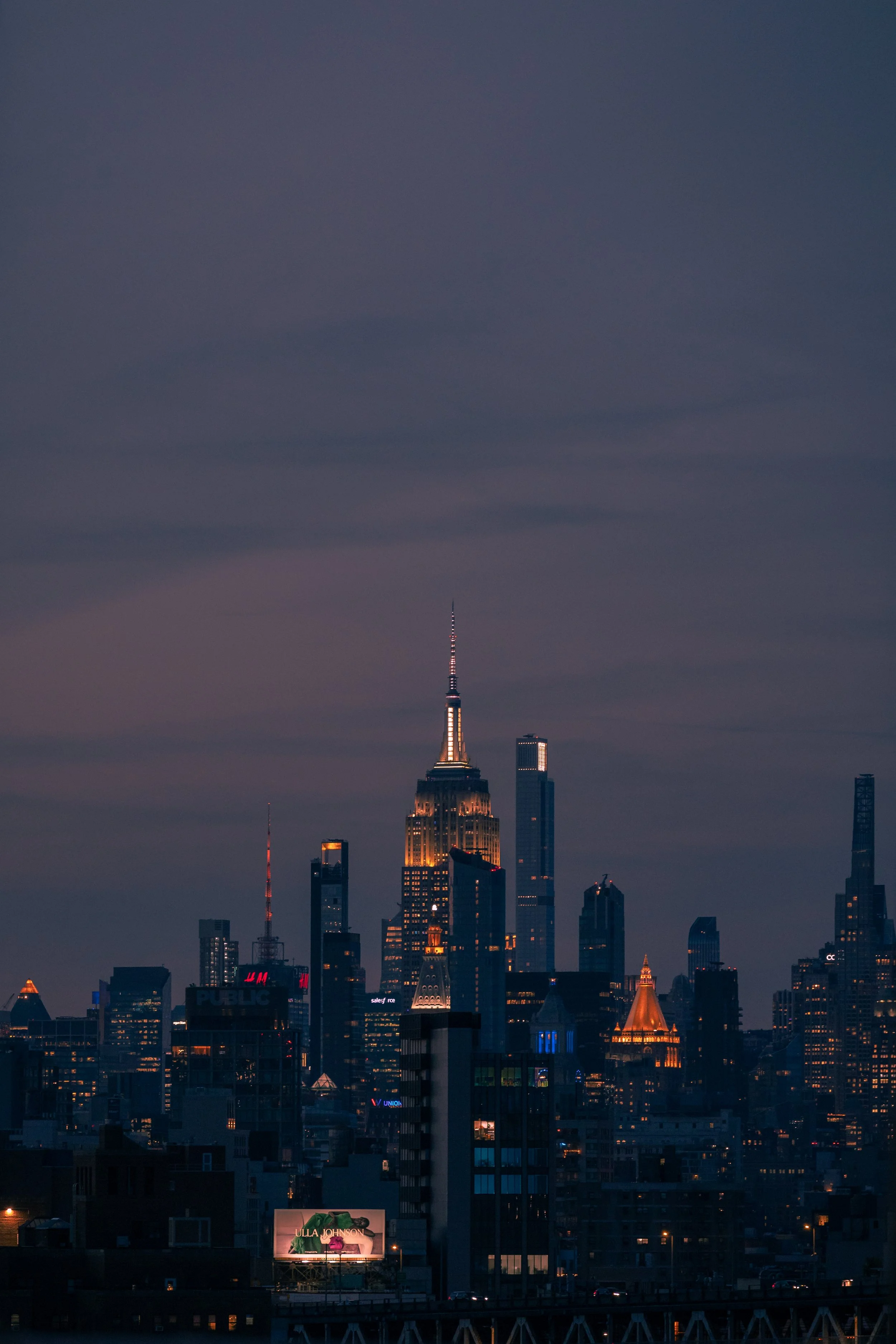 Nighttime city skyline with illuminated buildings, including the Empire State Building, under a dark sky.